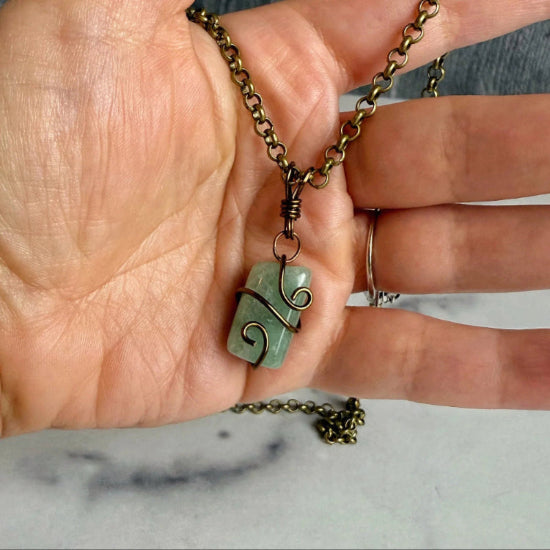 Hand holding a necklace with a green pendant against a wooden background