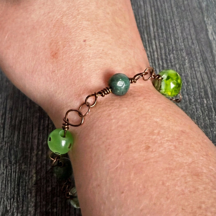 Hand wearing a bracelet with green beads on a wooden surface