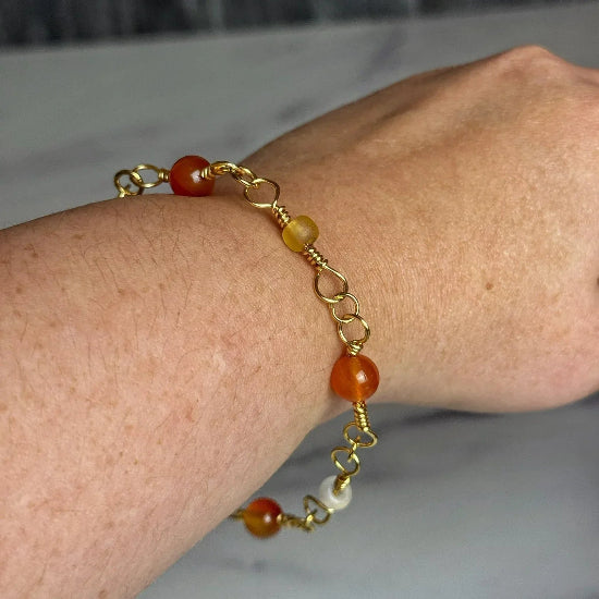 Gold bracelet with orange beads on a wrist against a neutral background