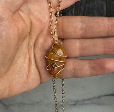 Hand holding a necklace with a stone pendant against a neutral background