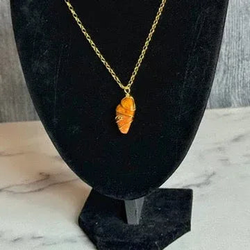 Gold necklace with a leaf-shaped pendant on a black stand.