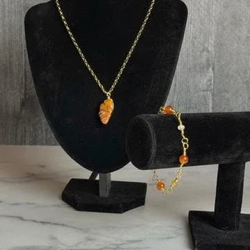 Necklace and bracelet with orange beads on black stands against a gray background