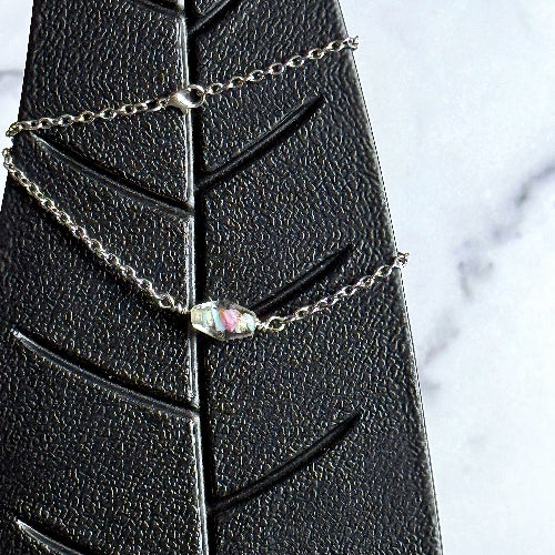Silver chain necklace with a central gemstone on a black leaf-shaped stand.