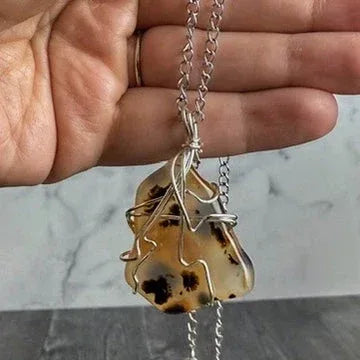 Hand holding a necklace with a unique pendant against a neutral background