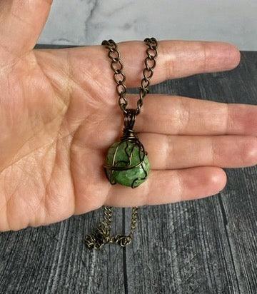Hand holding a necklace with a green stone pendant on a wooden surface