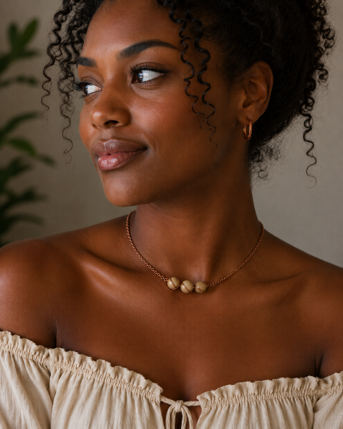 Woman wearing a beige off-shoulder top and a necklace with a neutral background