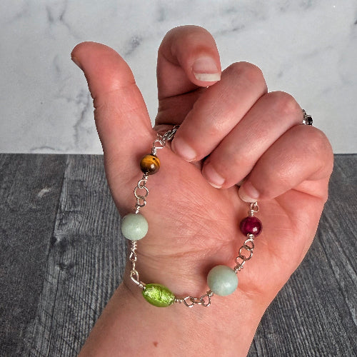 Hand holding a bracelet with colorful beads against a marble background