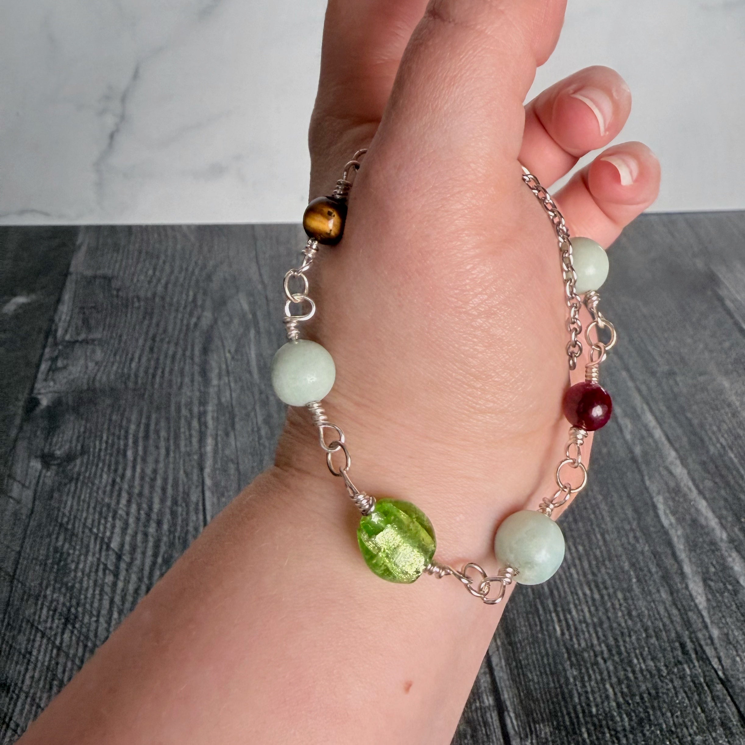 Hand wearing a bracelet with green, red, and white beads on a wooden surface