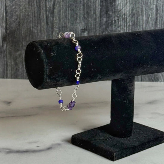 Bracelet with purple beads on a black stand against a wooden background