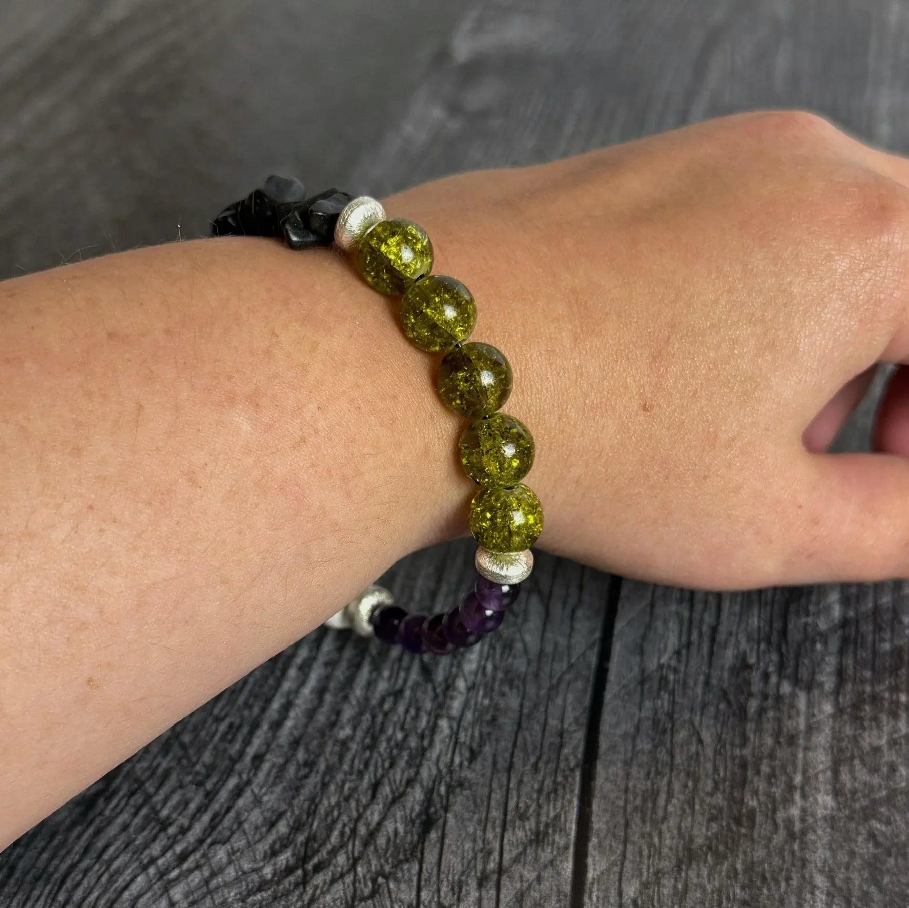 Beaded bracelet with green, black, and purple beads on a wrist against a wooden background