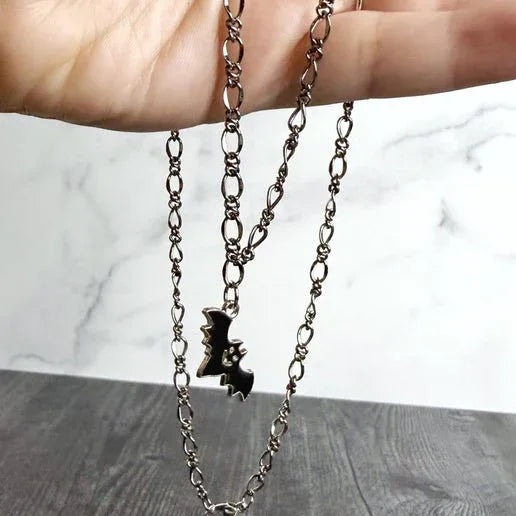 Necklace with a small bat pendant held by a hand on a marble surface