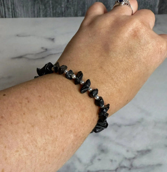 Hand wearing a black beaded bracelet on a marble surface