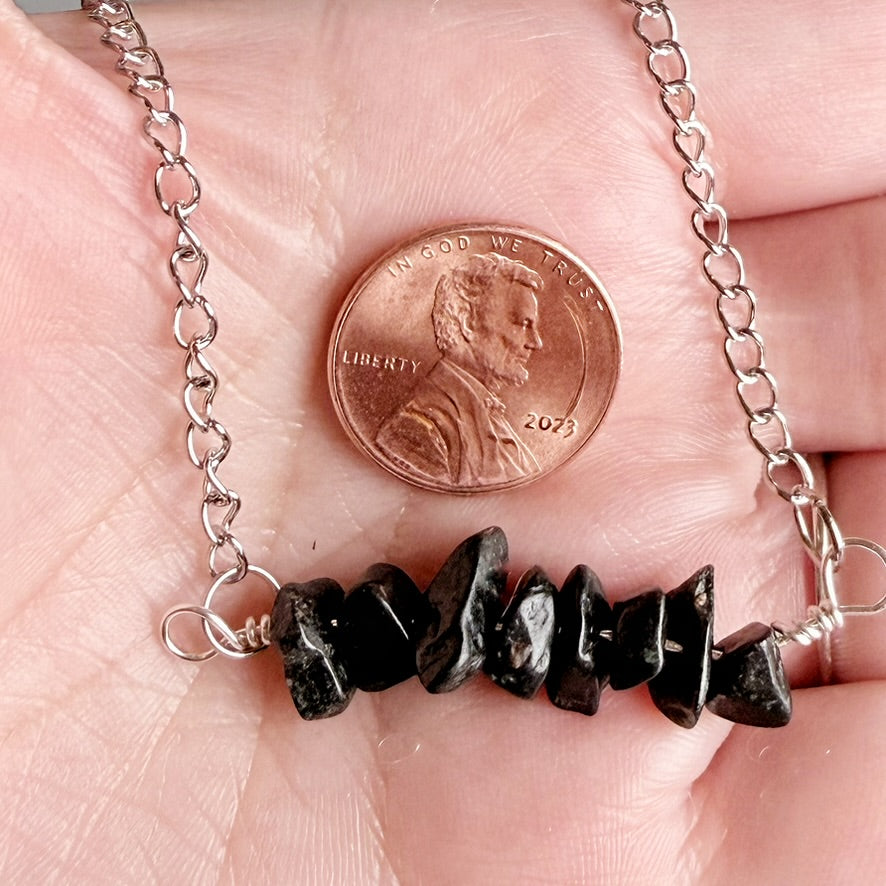 A close-up of a silver chain necklace draped across a person's palm, with a row of rough black beads strung across the center and a U.S.