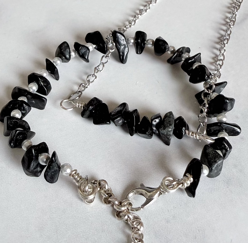 A silver chain necklace and bracelet set featuring polished black chip stones, displayed on a light gray marble surface.