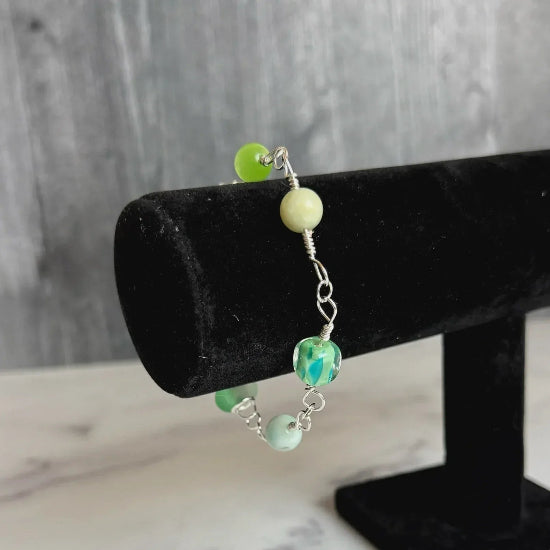 Bracelet with green beads on a black stand against a marble background