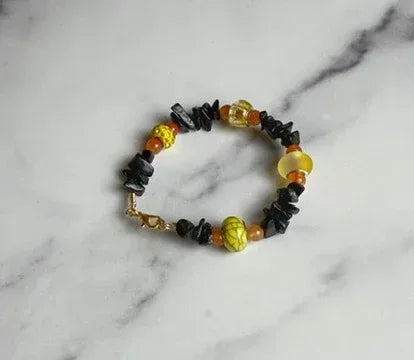 Bracelet with black, yellow, and orange beads on a marble background