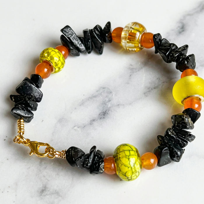 Bracelet with black, yellow, and orange beads on a marble background