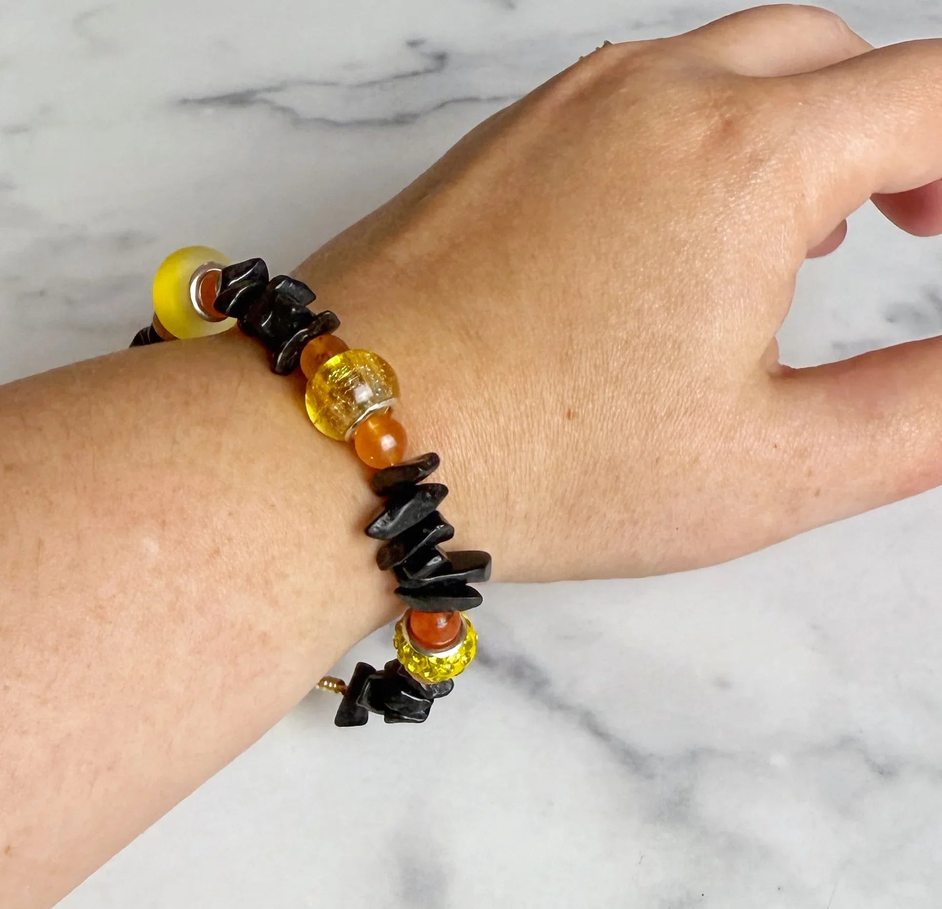 Bracelet with yellow, black, and orange beads on a wrist against a marble background
