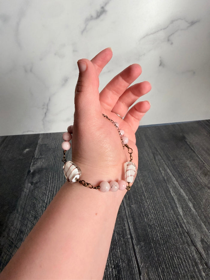 Hand wearing a pearl bracelet against a marble and wooden background