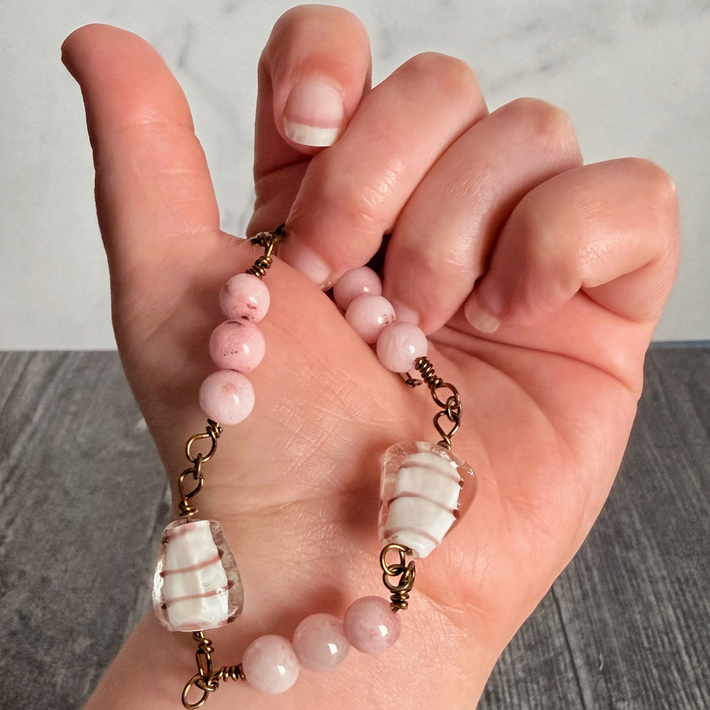 Hand holding a bracelet with pink beads and gold accents on a neutral background