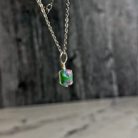 Necklace with a pendant featuring a green glass bead on a wooden background