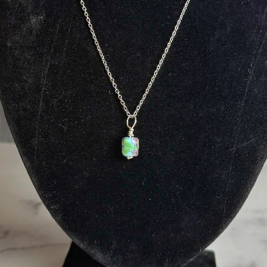 Necklace with a green pendant on a black bust against a marble and wooden background