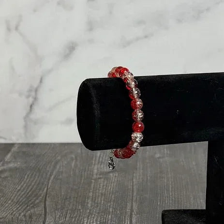 Red beaded bracelet on a black stand against a marble background