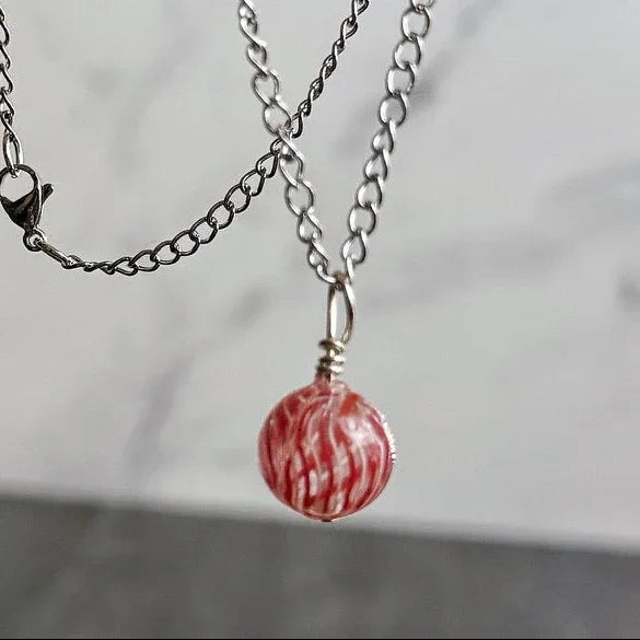 Silver chain necklace with a red marbled pendant held by a hand against a neutral background
