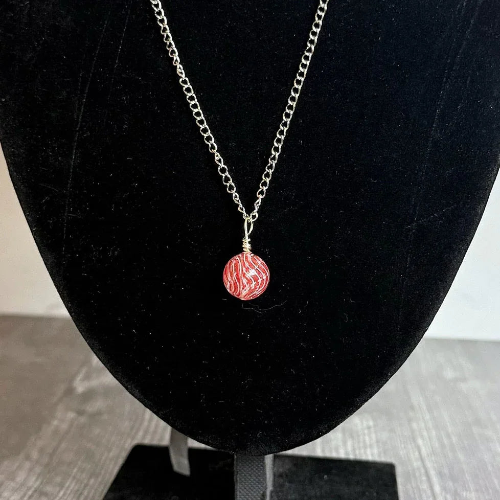 Necklace with a red pendant on a black velvet stand against a marble background