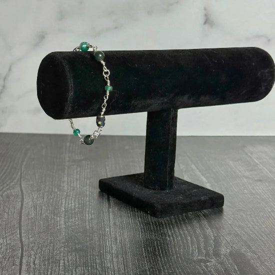 Bracelet with green beads on a black velvet stand against a marble background