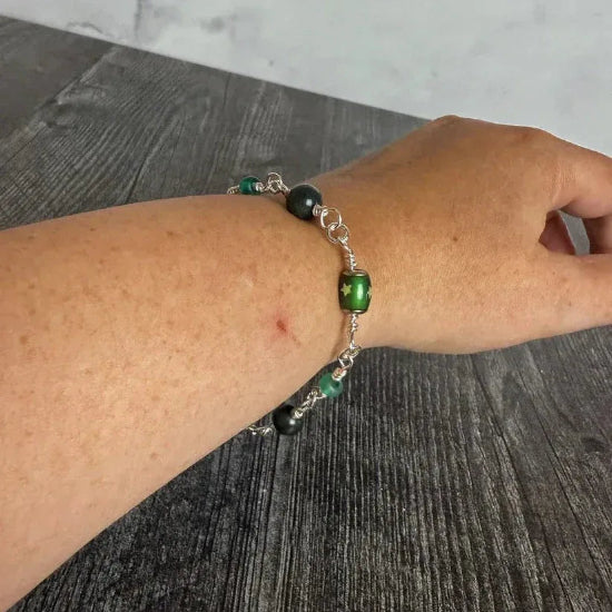 Hand wearing a bracelet with green beads on a wooden surface