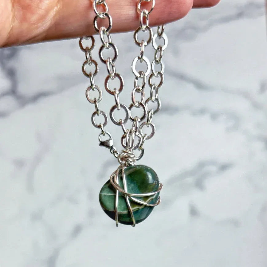 Necklace with a green stone pendant held by a hand on a marble background