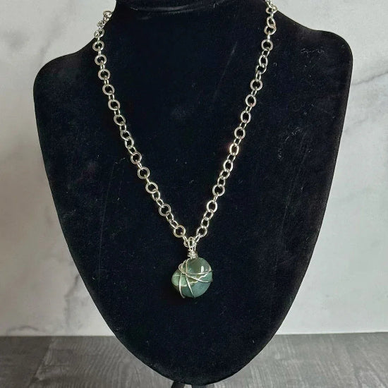Necklace with a green pendant on a black bust against a marble background
