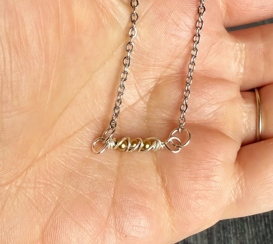 Silver necklace with a small pendant held in a hand.
