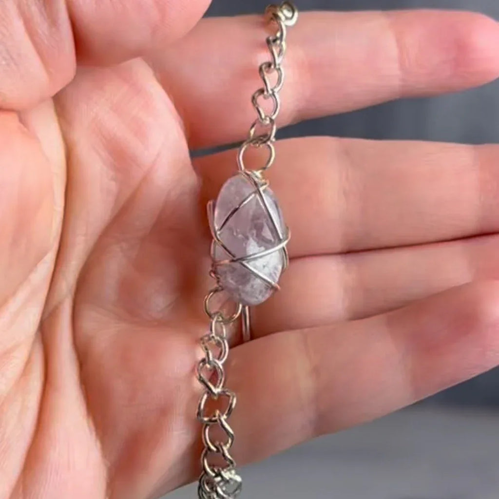 Hand holding a silver chain bracelet with an amethyst crystal bead against a neutral background