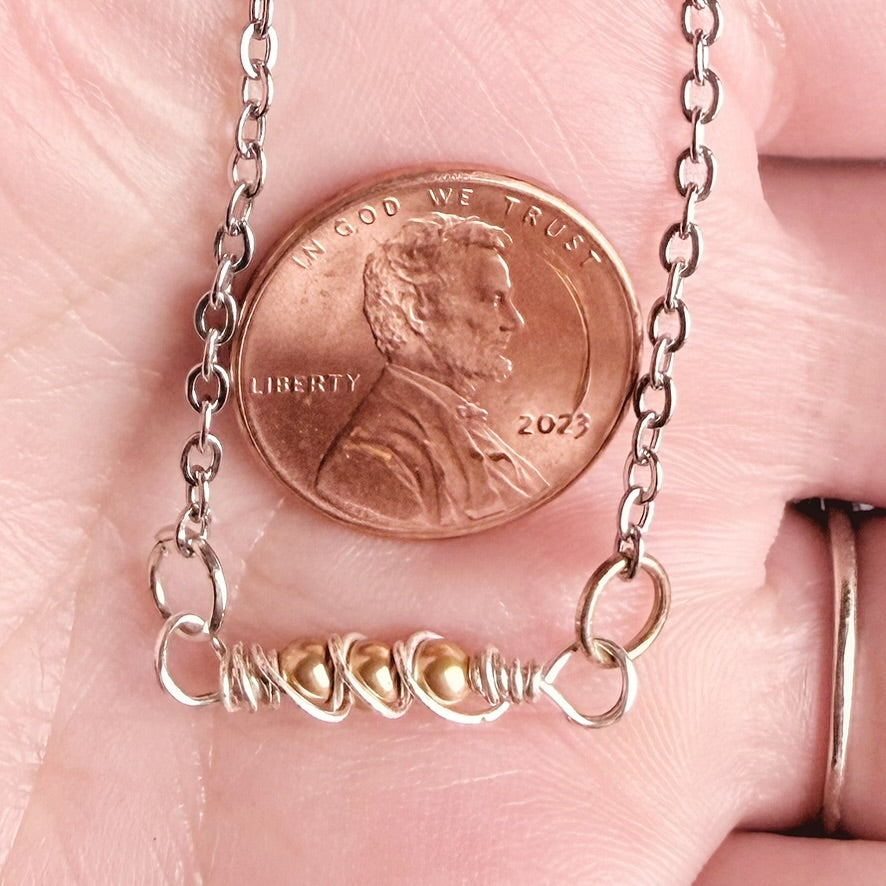 A close-up of a delicate necklace being held in a hand, with a U.S.