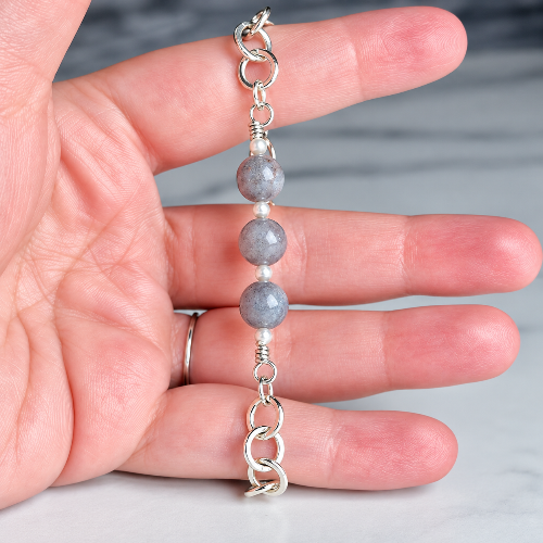 A handmade beaded bracelet with three gray stone beads and silver chain links, held in a person's hand to show scale.