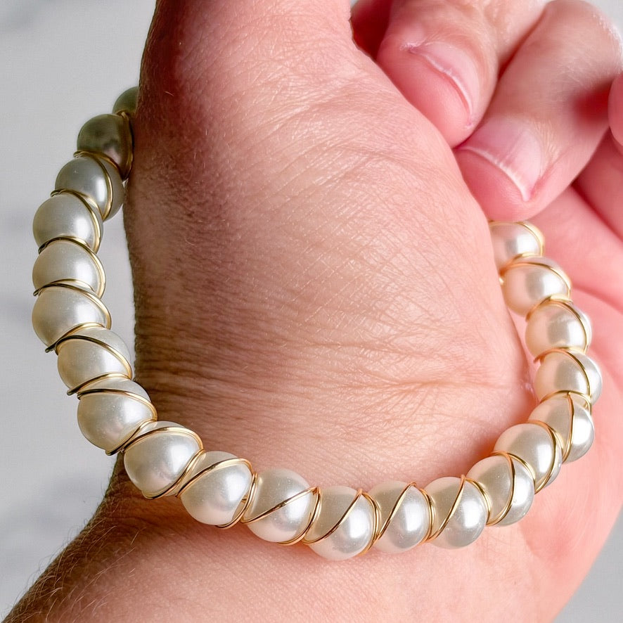 A close-up of a hand wearing a stretch bracelet made of irregular white pearls set in gold-tone metal.