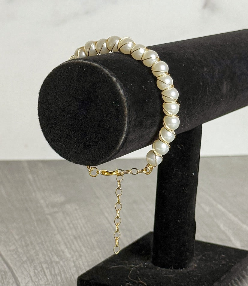 Pearl bracelet with a gold chain on a black stand against a neutral background
