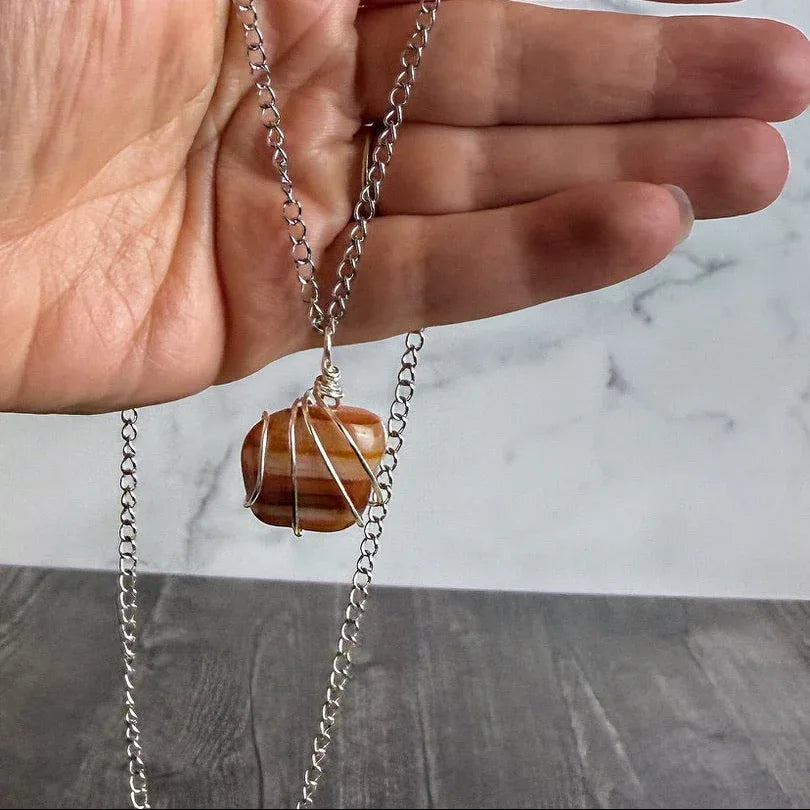 Hand holding a necklace with a carnelian stone pendant against a marble background
