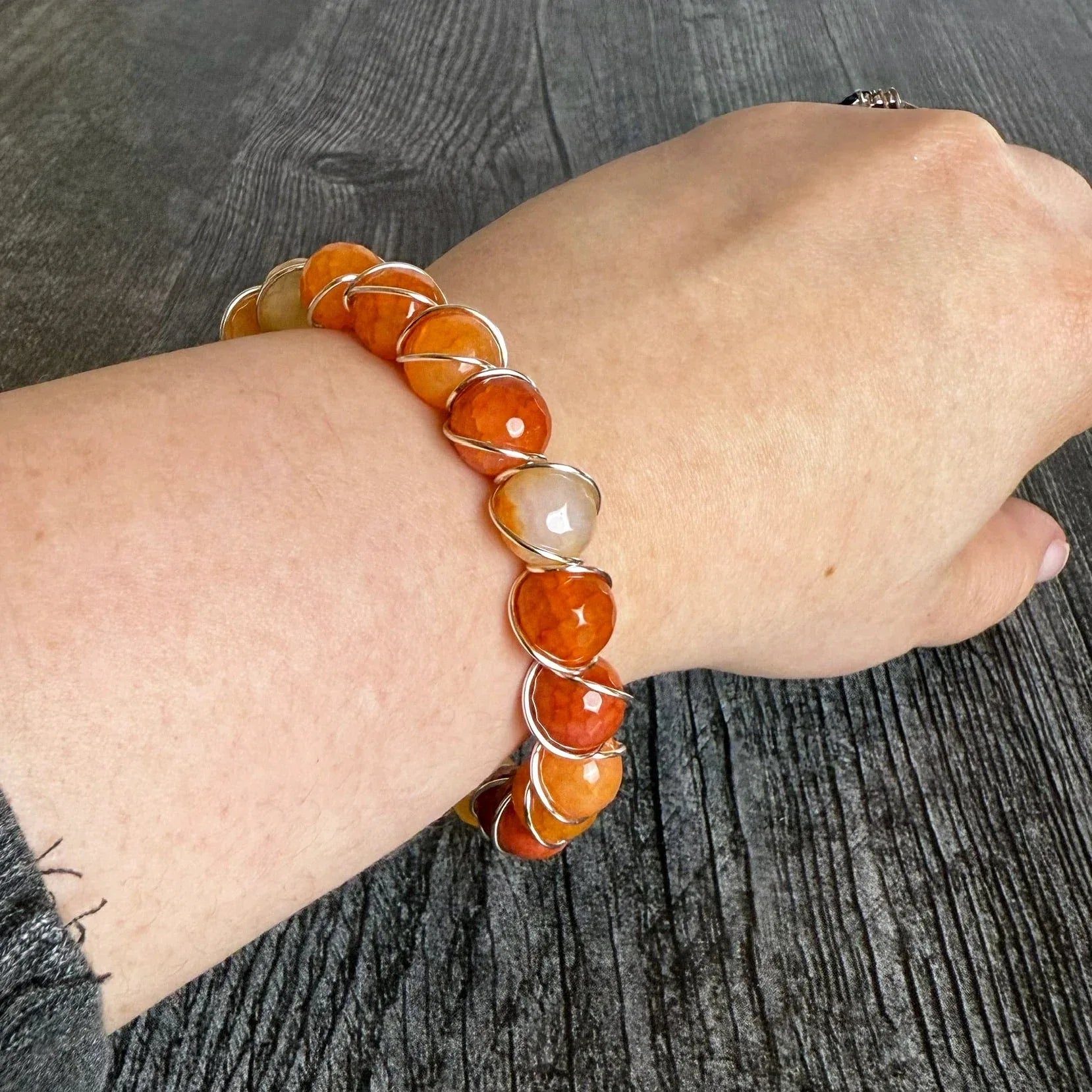 Bracelet with orange beads on a wrist against a dark textured background