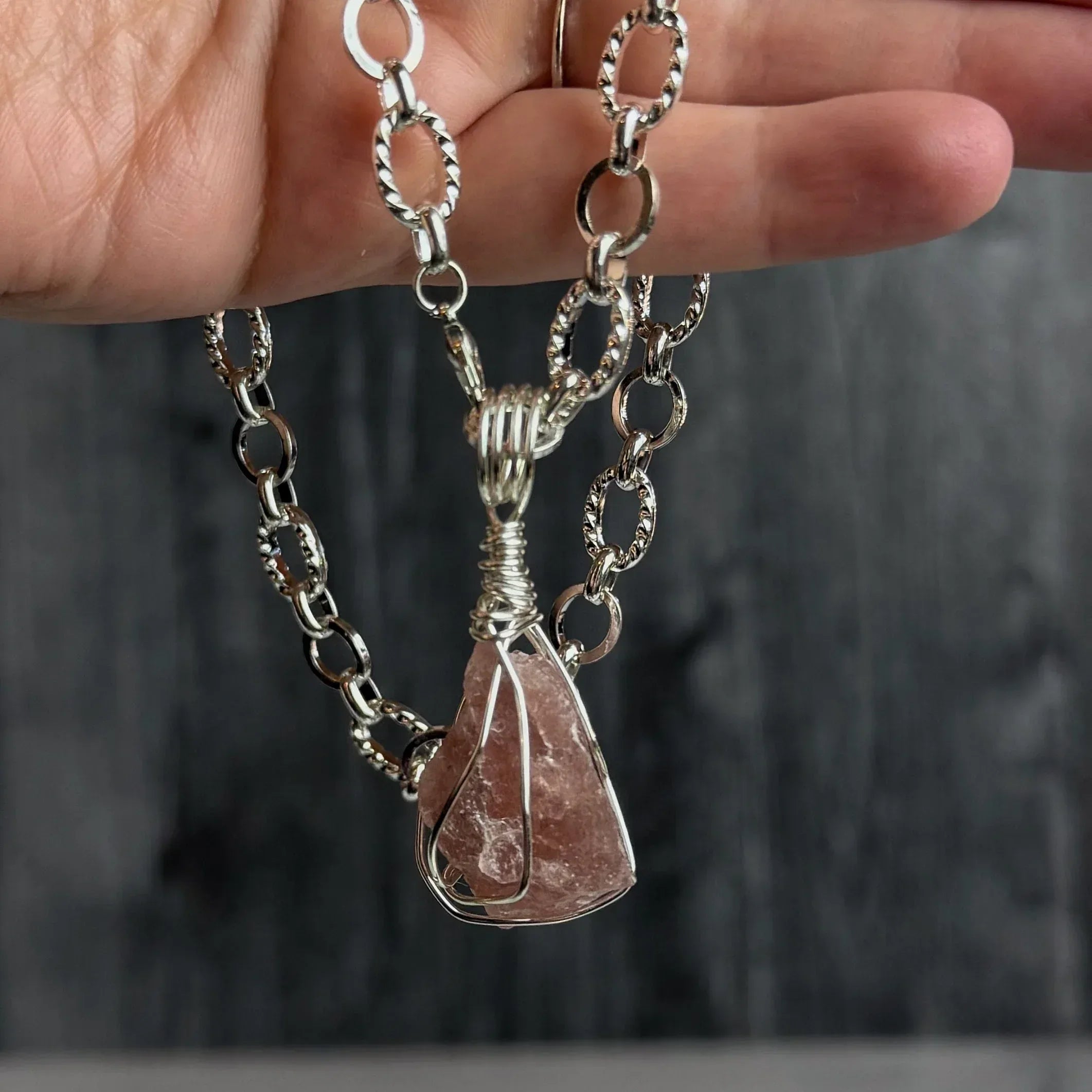 Silver chain necklace with a strawberry quartz stone pendant held by a hand against a dark background