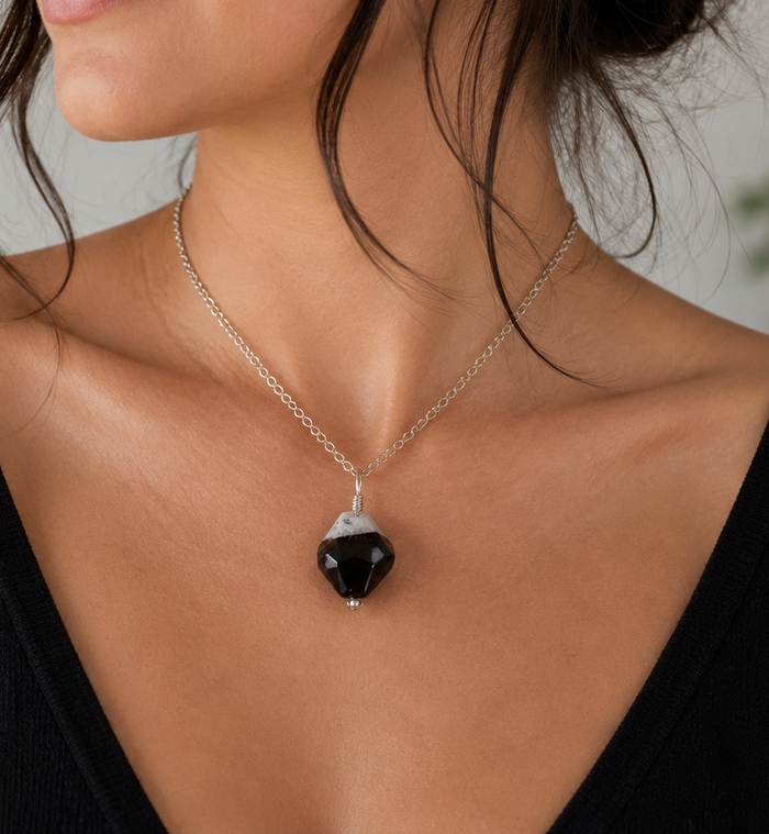 A woman wearing a silver chain necklace with a black teardrop-shaped pendant, shown in a close-up profile view.