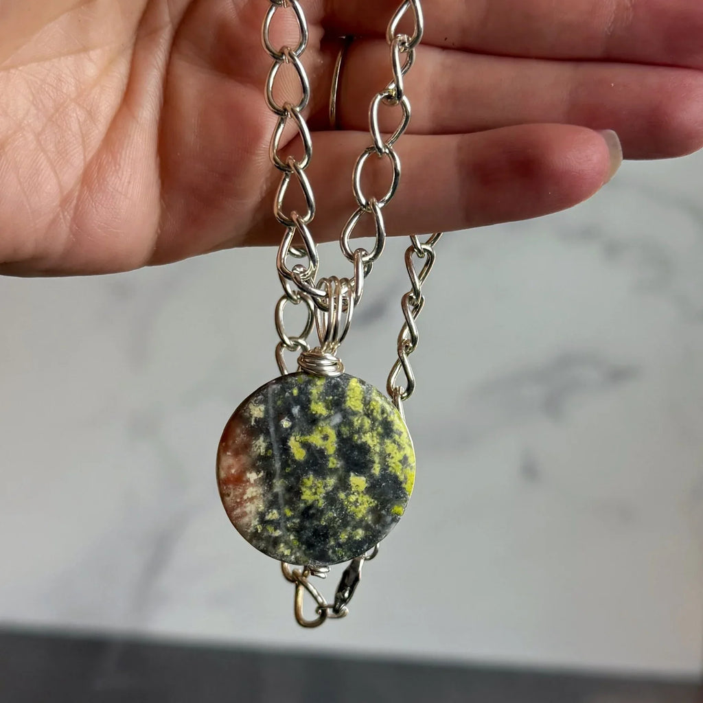 Necklace with a round, multicolored stone pendant held by a hand against a neutral background