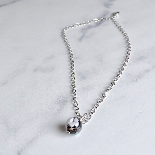 A delicate silver chain necklace with a small, polished silver bead pendant resting on a white marble surface.