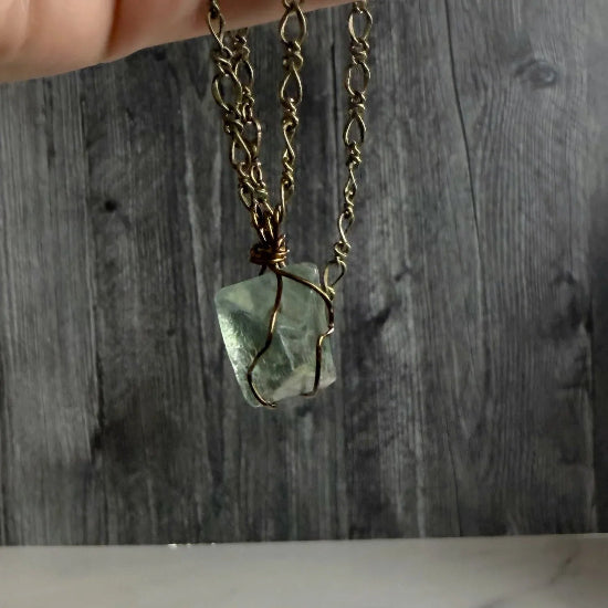 Necklace with a green stone pendant held by a hand against a wooden background