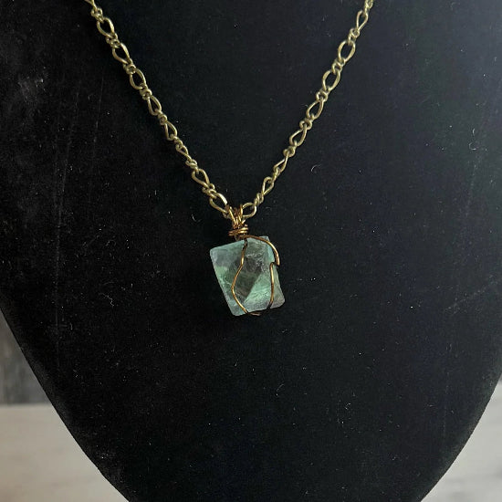 Necklace with a green pendant on a black mannequin bust against a gray wooden background.