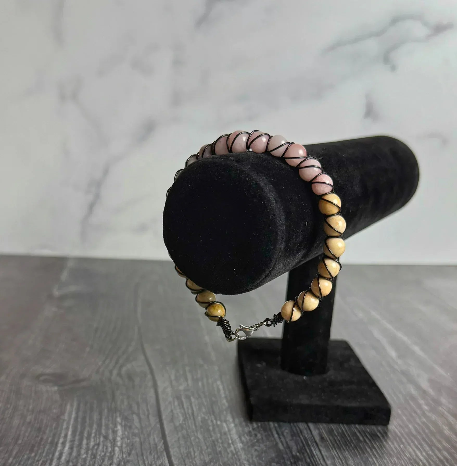 Bracelet with pink and beige beads on a black velvet stand against a marble background