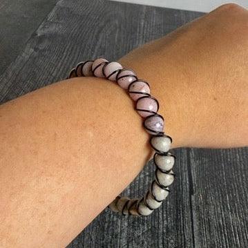 Bracelet with white and brown beads on a wrist against a dark wooden background