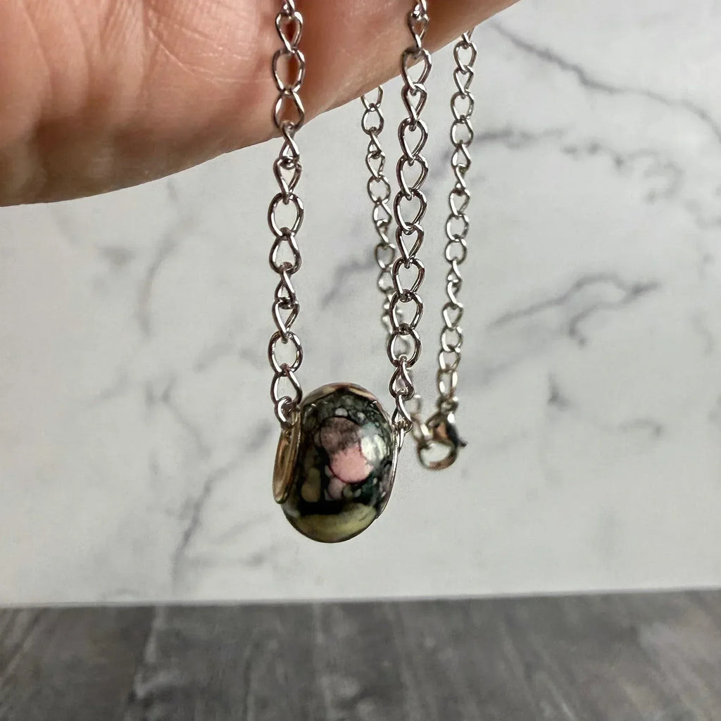 Necklace with a pendant held by a hand on a marble surface